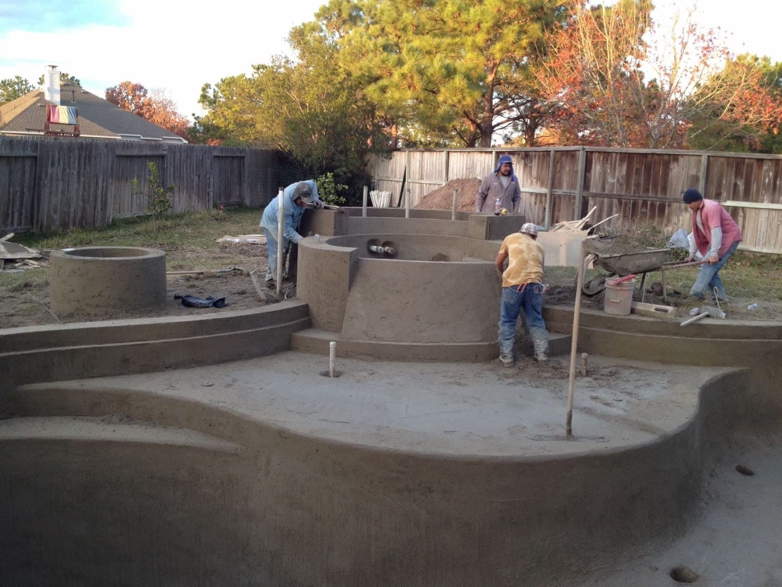 Four-man crew working a large pool and spa complex with raised spa shell and water feature base