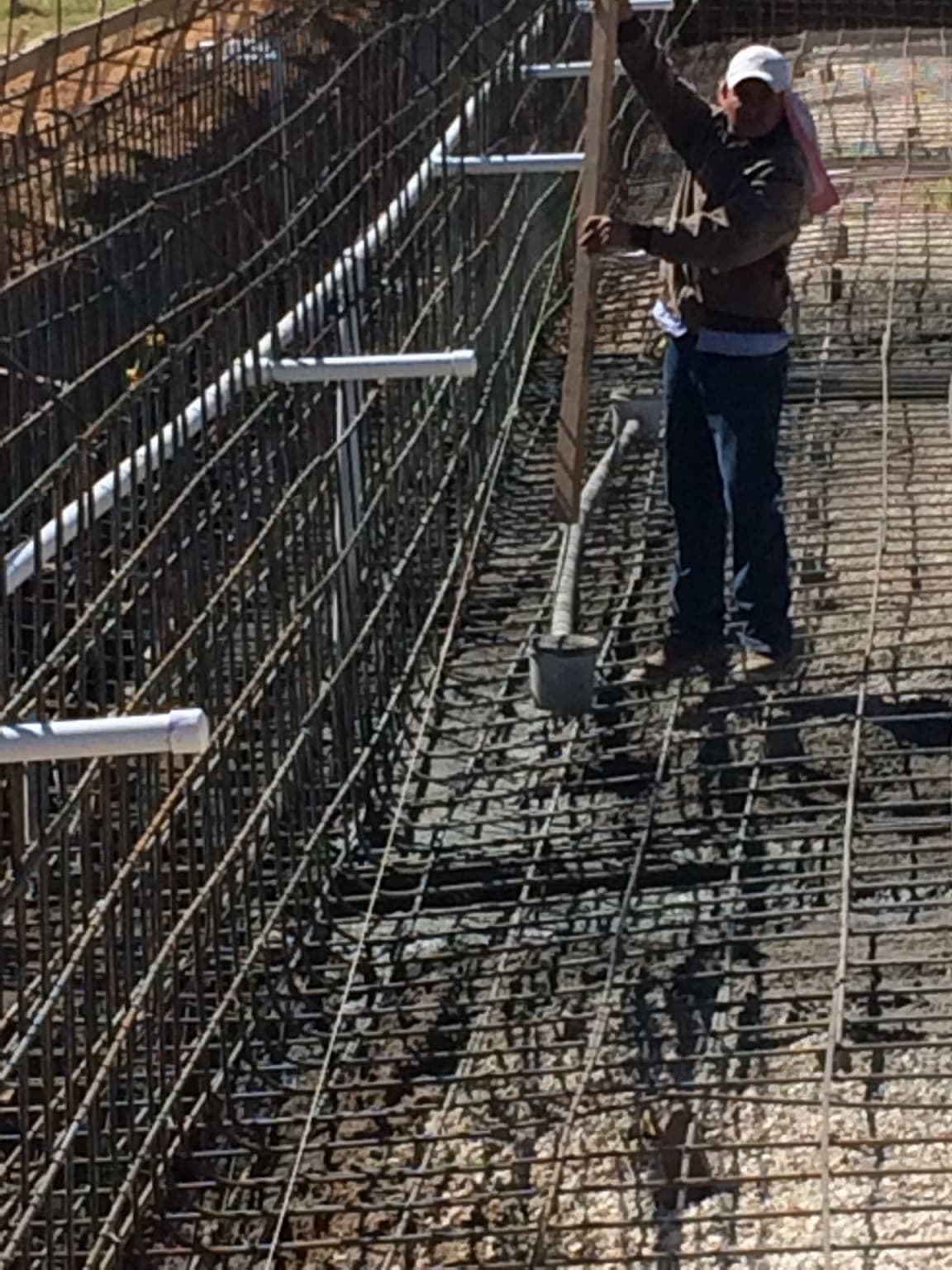 Worker checking rebar and plumbing layout on a large pool shell before gunite application