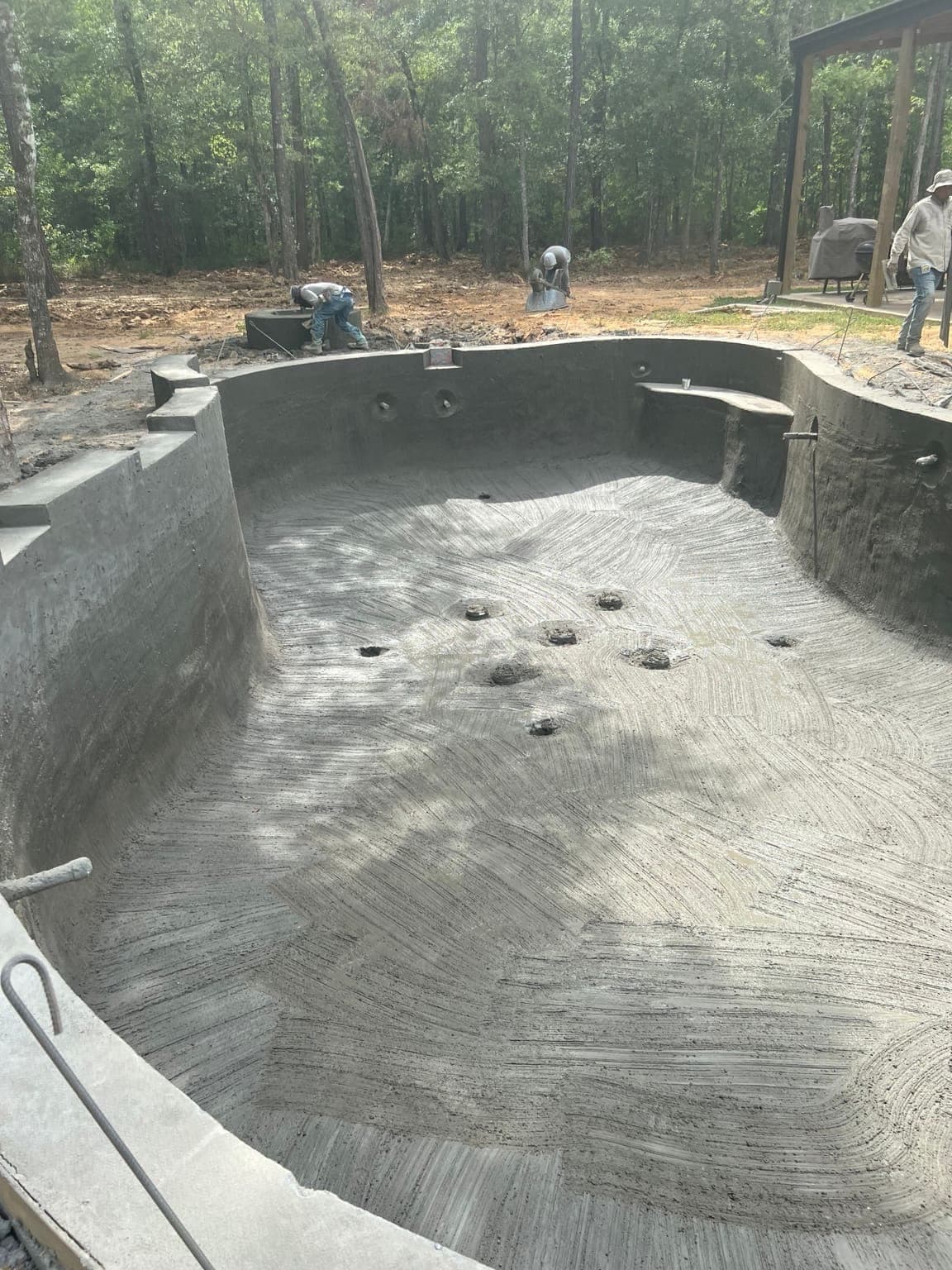 Freshly gunited freeform pool interior showing broom-finish texture, crew working in background