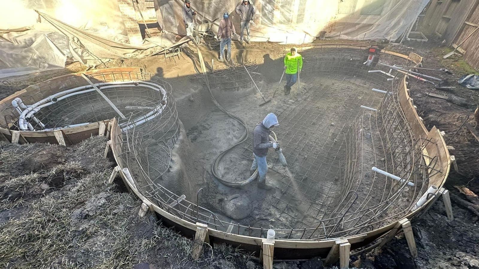 Elevated view of crew shooting gunite on a large freeform pool shell at dusk