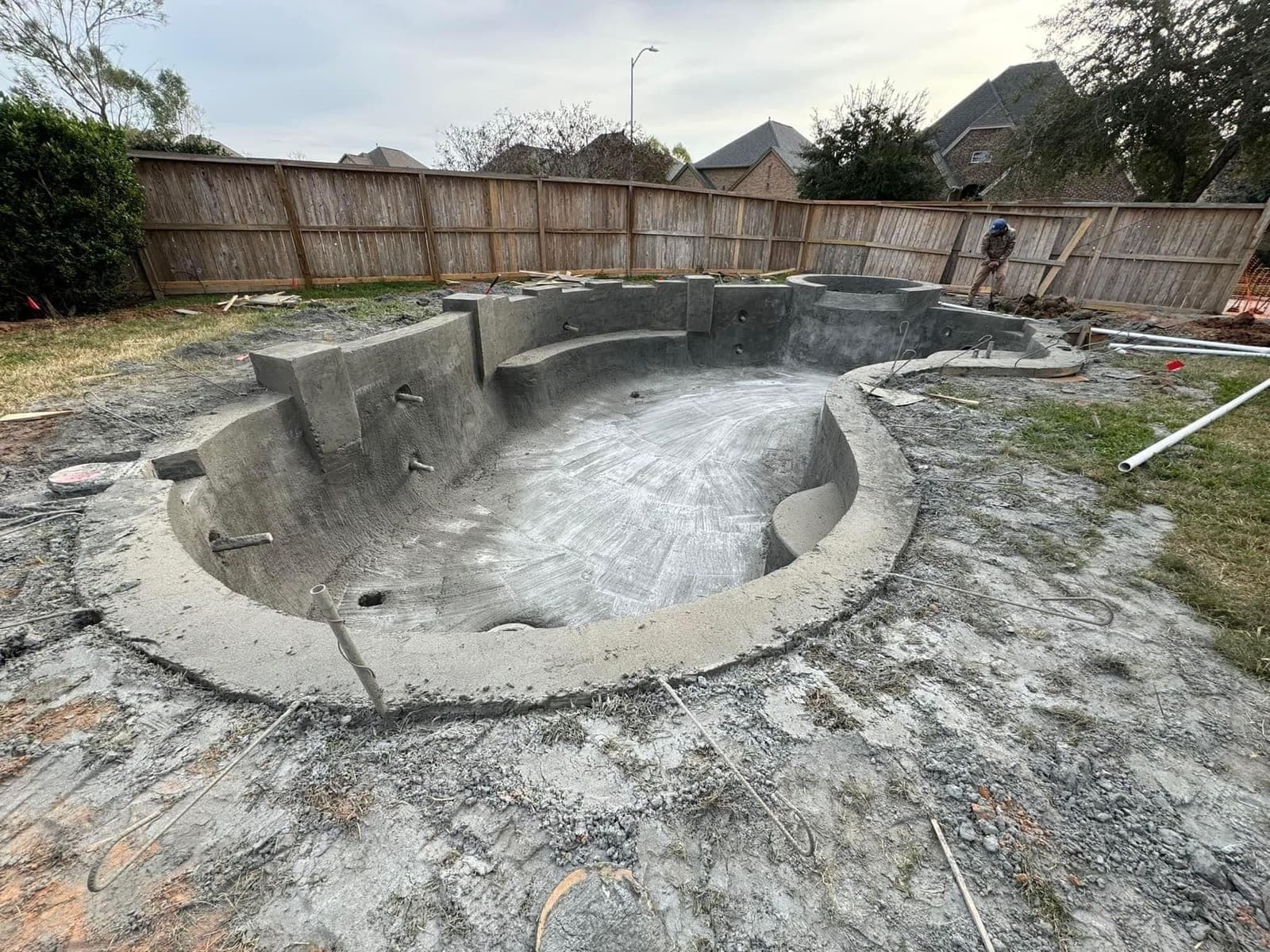 Freshly completed freeform gunite pool shell in a fenced suburban backyard, clean finish visible
